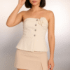 A woman modeling an elegant sleeveless white top with rosette and button details, paired with a premium beige skort, set against a soft neutral backdrop.